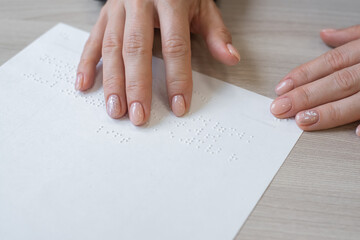 Close-up woman reads the text to the blind. Woman's hands on paper with braille code.