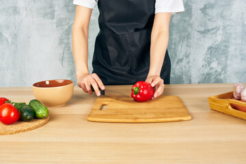 Woman in black apron on the kitchen cutting vegetables cutting board