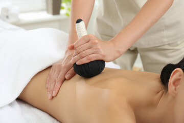 Young woman receiving herbal bag massage in spa salon, closeup