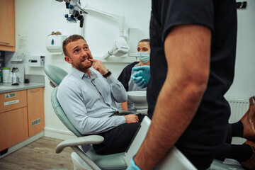 Fototapeta premium Caucasian male client explaining ache in tooth while sitting in dentist chair 