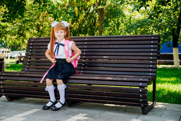 A schoolgirl in a white blouse and a black skirt with a briefcase is sitting on a bench in the...