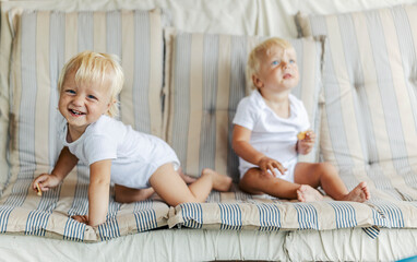 Baby twins are having fun. Two smiling toddlers in a white children's suit are sitting on a...