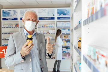 Fototapeta na wymiar Review of drugs by consumers, approval. An adult man stands elegantly dressed standing in the middle of the pharmacy and holding a bottle of supplements. In the background a blued female pharmacist