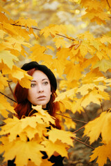 Naklejka na ściany i meble Pretty woman in park among the leaves. Autumn romantic portrait of a red-haired woman. Nature of the forest. Walk in fall Park.