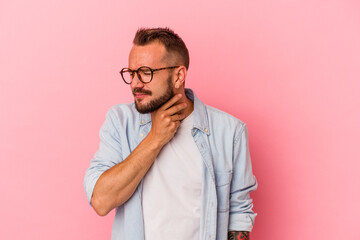 Young caucasian man with tattoos isolated on pink background  suffers pain in throat due a virus or...