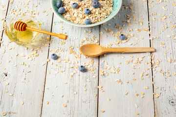 Bowl of oatmeal porridge with milk, honey and blueberry on vintage table top view in flat lay style. Hot breakfast and homemade food