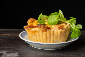 Close-up of mushroom quiche with lamb's lettuce, selective focus, on dark wooden table, black background, horizontal, with copy space