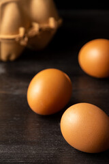 Top view of three brown eggs with cardboard box, selective focus, on dark wooden table, vertical