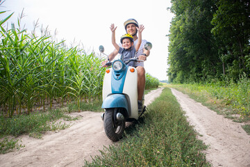 The father and son riding together through the field by pathway on the retro scooter