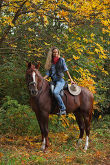 Beautiful cowgirl ride her horse in autumn country road at sunset