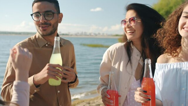 Slow motion portrait of happy youth dancing outdoors on beach holding bottles with drinks talking laughing having fun together. Youth and beverage concept.