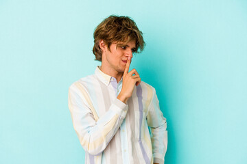Young caucasian man with make up isolated on blue background  keeping a secret or asking for...