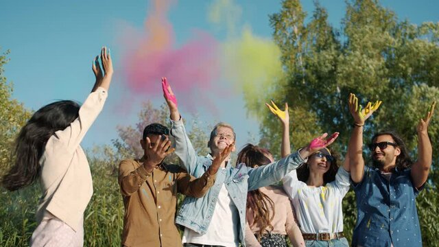 Slow motion of happy young people throwing colorful powder paint during Indian Holi festival laughing and having fun enjoying tradition outdoors in park.