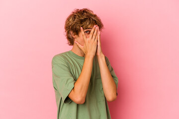 Young caucasian man with make up isolated on pink background blink through fingers frightened and nervous.