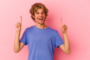 Young caucasian man with make up isolated on pink background indicates with both fore fingers up...