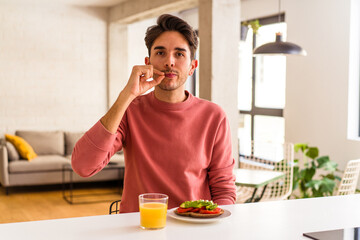 Fototapeta na wymiar Young mixed race man having breakfast in his kitchen with fingers on lips keeping a secret.