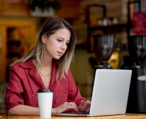 young woman using laptop computer drink a coffee sits at table in a cafe