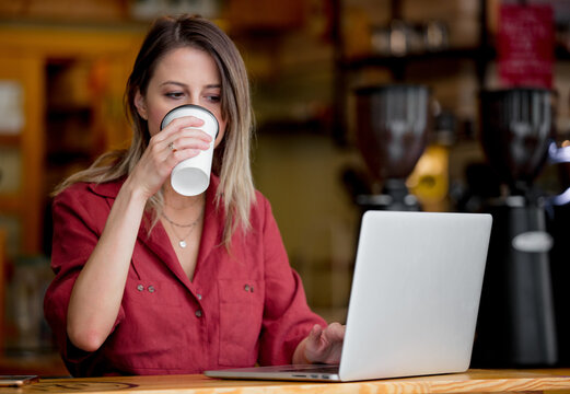 young woman using laptop computer drink a coffee sits at table in a cafe