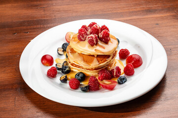Pancakes with caramel and seasonal berries on a wooden backdrop. Breakfast