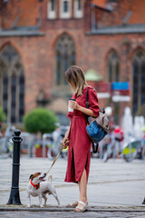 young woman walking a dog in the city while drinking coffee