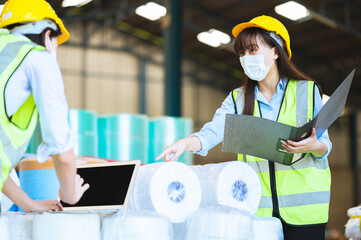 Team engineers and foreman or technicians males and females wear a mask, hard hat and vest. Standing, consult discuss industrial production management through data files within the factory.
