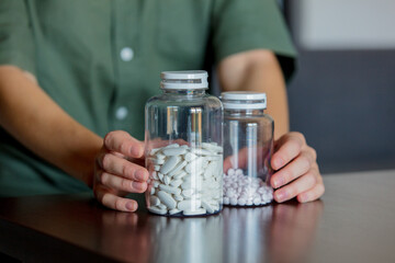 Woman holds two jars of white pills on a table at home
