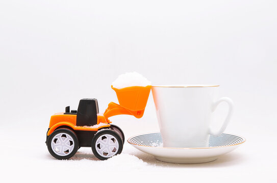 A Miniature Toy Tractor Plowing, Lifting Granulated Sugar Into A Cup With A Drink, Tea Or Coffee On A White Background. Giving Up Sugar