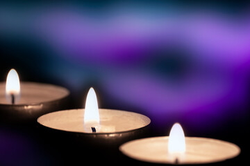 Three burning yellow candles on blurry purple background with copy space. Christmas candlelight in...