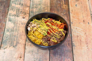 Poke bowl of red tuna fuji with mango, pieces of mushrooms, ripe avocado and salad of cherry tomatoes, carrots and white rice base