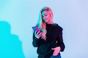 Happy beautiful girl with a smile in a fashion black hoodie and blue jeans holds a smartphone and...
