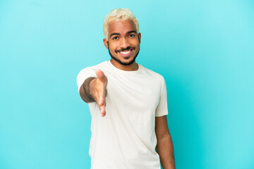 Young Colombian handsome man isolated on blue background shaking hands for closing a good deal