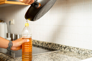 Close up of a man's hands recycling edible oil from a frying pan into a plastic bottle in his home...