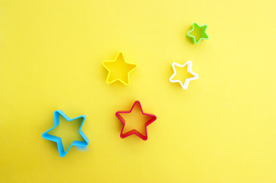 Plastic molds of multi colors for making cookies in the shape of a star on a yellow background.