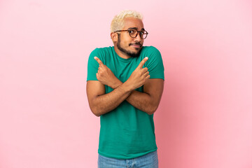 Young Colombian handsome man isolated on pink background pointing to the laterals having doubts