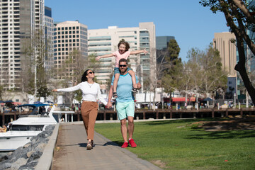 Portrait of happy young family holding hands walking with their child on the city. People urban...