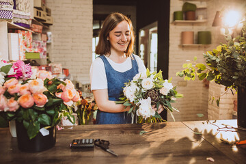 Woman florist at her own floral shop taking care of flowers - obrazy, fototapety, plakaty
