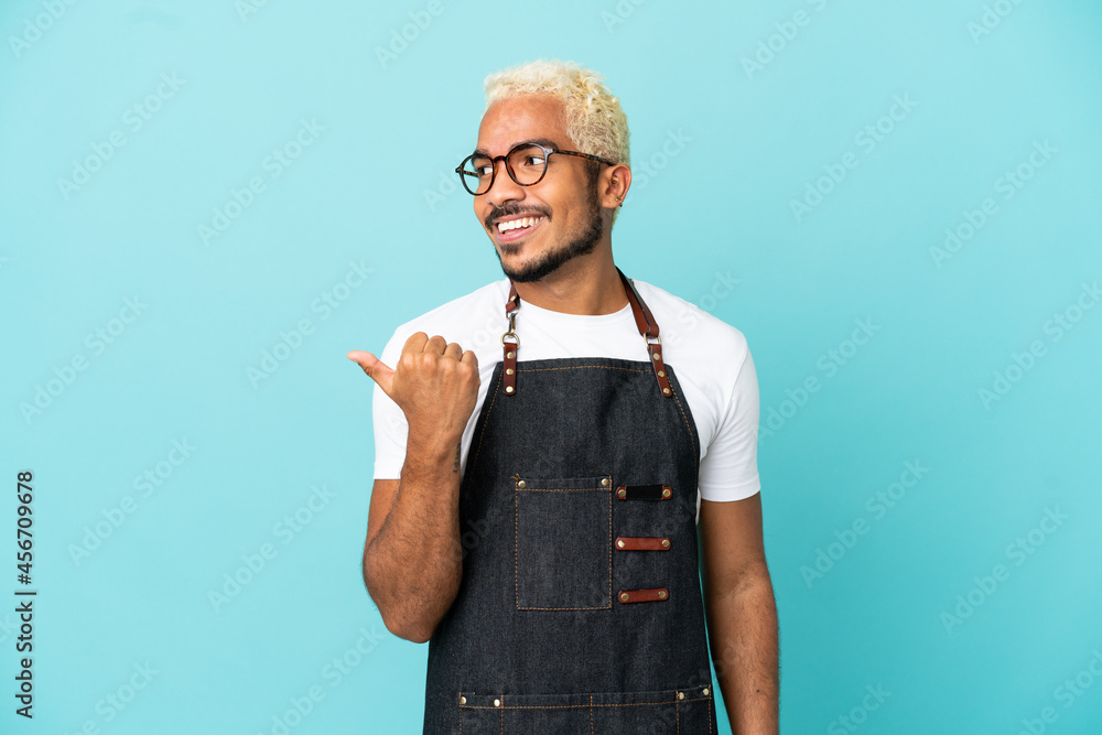 Wall mural restaurant colombian waiter man isolated on blue background pointing to the side to present a produc