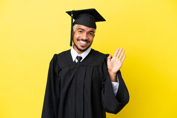 Young university graduate Colombian man isolated on yellow background saluting with hand with happy expression