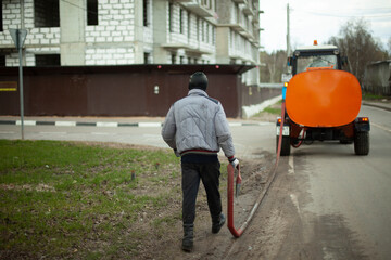 A worker washes the road from a hose. Cleaning of the territory. Washing off dirt from asphalt.