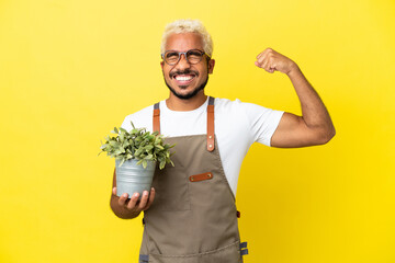 Young Colombian man holding a plant isolated on yellow background doing strong gesture