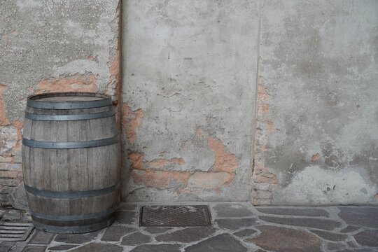 Old wooden barrel against a rustic wall pattern and on a stone pavement outdoors.