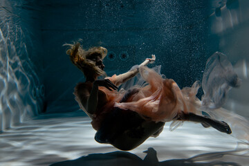 A girl with long dark hair swims underwater in a pink dress and with a crown on her head, like an underwater queen. Fairy tale suitable for advertising	