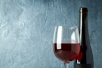 Bottle and glass of red wine against blue textured background