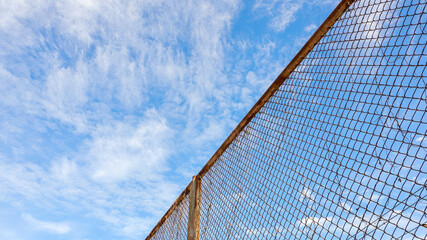 Rust steel mesh iron hain fence with sky background.