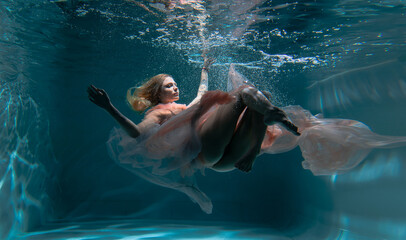 A girl with long dark hair swims underwater in a pink dress and with a crown on her head, like an underwater queen. Fairy tale suitable for advertising	