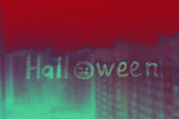 Fototapeta premium Handwritten lettering green Halloween with scary face on rainy red glass window with raindrops