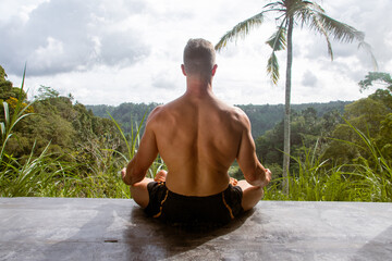 Yogi man sitting in lotus position on the background of the jungle