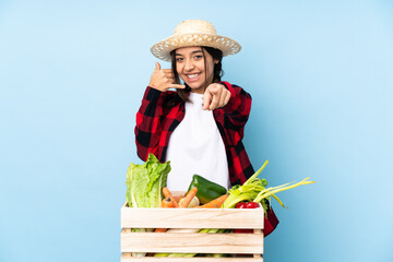Young farmer Woman holding fresh vegetables in a wooden basket making phone gesture and pointing...