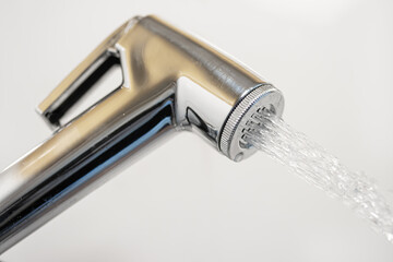 A chrome bidet shower spraying water, close up. - obrazy, fototapety, plakaty