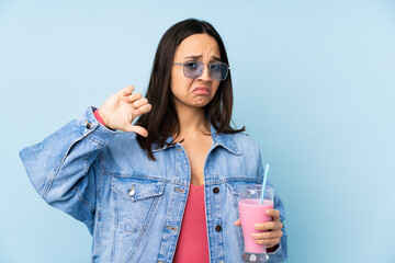 Young woman with strawberry milkshake over isolated blue background showing thumb down